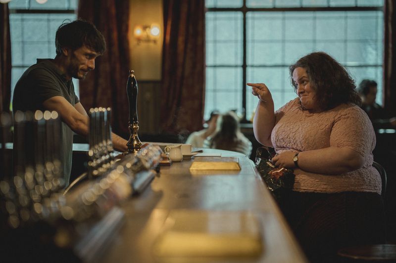 Richard Gadd and Jessica Gunning look at each other across the bar in a pub in Baby Reindeer. She’s pointing at him and smiling